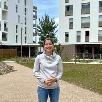 une femme blonde dans un jardin avec un immeuble blanc en fond